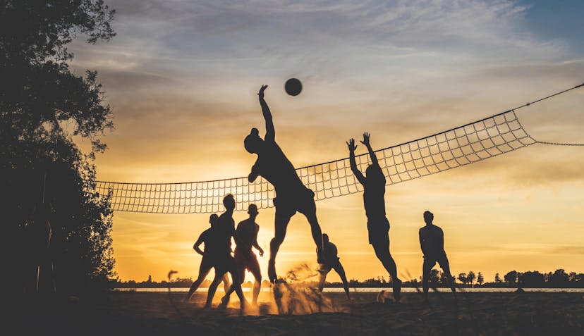 Menschen die Volleyball im Sonnenuntergang spielen